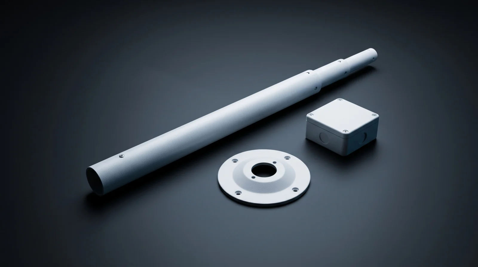 A white telescoping camera pole, a round ceiling mounting plate and a small junction box arranged on a dark surface.